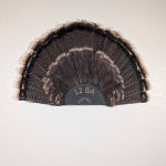 Kabash Outdoors American steel turkey fan display hanger. Fan holder is textured black and looks like the end of a 12ga shotgun shell. It is holding a beautiful turkey tail.