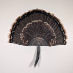 Kabash Outdoors American steel turkey fan display hanger. Fan holder is textured black and looks like a tree stump. It is holding a beautiful turkey tail and beard.