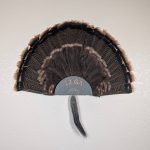 Kabash Outdoors American steel turkey fan display hanger. Fan holder is hammered silver and looks like the end of a 12ga shotgun shell. It is holding a beautiful turkey tail and beard.