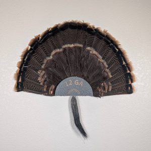 Kabash Outdoors American steel turkey fan display hanger. Fan holder is hammered silver and looks like the end of a 12ga shotgun shell. It is holding a beautiful turkey tail and beard.